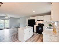 Open kitchen with white cabinets, black appliances, island, and hardwood floors into the living room at 301 Walkers Ridge Dr, Shelby, NC 28152