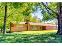 Inviting single-story brick home with a neatly landscaped front yard, framed by mature trees and a chimney at 6447 E Nc 27 Hwy, Iron Station, NC 28080
