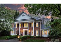 Elegant brick home featuring stately columns, mature landscaping, and a beautifully lit facade at twilight at 6824 N Baltusrol Ln, Charlotte, NC 28210