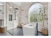 Bright bathroom featuring marble walls, black pebble tile, soaking tub and glass shower with a rainfall shower head at 18730 Floyd Ct, Davidson, NC 28036