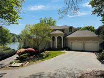 Beautiful beige home featuring a two-car garage, arched entryway, lush landscaping, and partial lake view at 255 Charlotte Ann Ln, Hickory, NC 28601