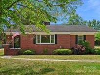 Charming one-story brick home featuring a well-maintained lawn and mature landscaping, American flag near entry at 613 W Pine St, Kershaw, SC 29067