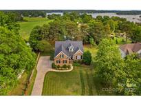 Stunning aerial view of a brick home with a well-manicured lawn and mature trees near the water at 7923 Mountain Shore Dr, Sherrills Ford, NC 28673
