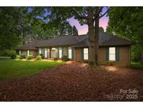 Charming brick home with green shutters, a lush lawn and mature trees at dusk at 8368 Fairfield Forest Rd, Denver, NC 28037