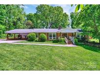 Charming brick ranch home with lush lawn, carport, and inviting front porch nestled among mature trees at 3810 Springway Dr, Gastonia, NC 28056