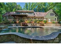 View of a large pool and stone patio area that backs up to the house with lots of shrubbery and foliage at 8400 Prince Valiant Dr, Waxhaw, NC 28173