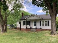 Quaint exterior of a home with a covered porch and black shutters, framed by mature trees in a green yard at 4630 Roberta Rd, Concord, NC 28027