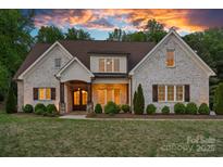 Charming brick home featuring manicured landscaping, warm exterior lighting, and a beautiful sunset backdrop at 2309 Ethan Way, Weddington, NC 28104