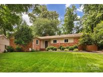 Charming single-story brick home with a lush green lawn, mature trees, and landscaped garden beds in the front yard at 1514 Wensley Dr, Charlotte, NC 28210