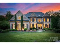 Stately brick home with manicured lawn, mature trees and lush landscaping during a beautiful twilight at 1021 Westbury Dr, Matthews, NC 28104