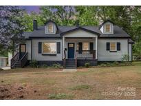 Charming bungalow-style home featuring a covered porch, black shutters, dormers, and mature trees at 1208 Fordham Rd, Charlotte, NC 28208