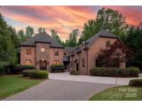 Stunning two-story home with stone accents, lush landscaping, and a paver driveway, set against a vibrant sunset sky at 1504 Alydar Ct, Waxhaw, NC 28173