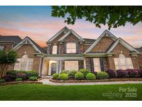 Beautiful brick and stone home with lush landscaping and manicured lawn at sunset, perfect for Gathering living at 10205 Alouette Dr, Waxhaw, NC 28173
