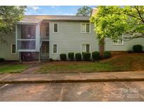 View of the two-story condo with light-grey siding, trimmed shrubbery, and stairs to the second floor entrance at 2026 Harvest Ln, Charlotte, NC 28210