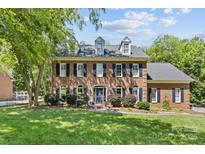 Charming two-story brick home featuring black shutters, dormers, mature landscaping, and a well-manicured lawn at 9513 Tresanton Dr, Charlotte, NC 28210