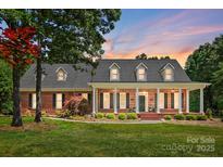 Charming brick home with a covered front porch, white columns, and meticulously landscaped front yard at sunset at 4570 Chanel Ct, Concord, NC 28025