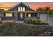 Charming gray home with a cozy front porch and well-manicured landscaping at sunset at 225 N Main St, Mount Pleasant, NC 28124