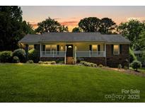 Charming ranch-style home with a brick facade, covered porch, and lush front lawn at sunset at 3712 Eaglebrook Dr, Gastonia, NC 28056