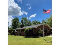 Charming brick home featuring a manicured lawn, mature trees, and an American flag at 211 Amos Homesley Rd, Cherryville, NC 28021