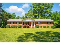 Charming brick home with a manicured lawn and lush landscaping under a sunny, blue sky at 6215 Simpson Rd, Charlotte, NC 28216