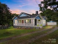 Charming cottage style home with a welcoming front porch, lush landscaping, and detached garage at 1001 Old Charlotte Rd, Concord, NC 28027