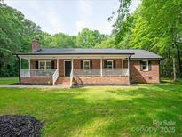 Charming brick ranch with a welcoming front porch, complemented by a lush green lawn and mature trees at 300 Hugh Crocker Rd, Matthews, NC 28104