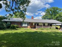 Charming brick home featuring a metal roof, covered front porch, and a spacious green lawn at 180 Needmore Rd, Woodleaf, NC 27054