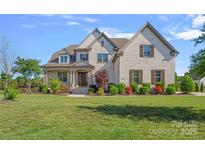 Stately brick home featuring a manicured lawn, attractive landscaping, and a covered front porch at 409 Wheatberry Hill Dr, Matthews, NC 28104