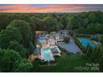 Expansive estate featuring a luxurious pool area, lush landscaping, and a distant city skyline at sunset at 8300 Fairview Rd, Charlotte, NC 28226