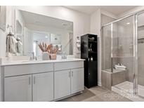 Modern bathroom featuring a double sink vanity, large mirror, black cabinet, and tiled glass door shower at 4229 Summit Woods Dr, Charlotte, NC 28216