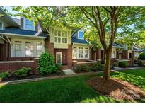 Charming brick townhome featuring lush landscaping, a covered front porch, and a well-manicured lawn at 6312 Mission Pl, Charlotte, NC 28210