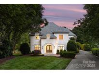 Elegant home featuring an arched entryway, meticulous landscaping, and a gray shingle roof set against a pastel sunset at 15038 Jockeys Ridge Dr, Charlotte, NC 28277
