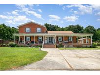 Charming two-story red brick home with a spacious wraparound porch and well-manicured lawn at 907 Sikes Mill Rd, Monroe, NC 28110