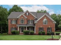 Charming two-story red brick home featuring black shutters, a well-manicured lawn, and lush landscaping at 601 Carver Pond Ln, Waxhaw, NC 28173