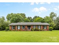 Charming single story brick home with a well-maintained lawn, mature trees and green shutters at 124 Courtney Ln, Matthews, NC 28105