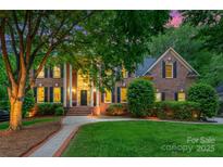 Elegant brick home featuring a columned entryway, manicured lawn, and lush landscaping with mature trees at 7812 Seton House Ln, Charlotte, NC 28277