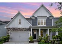Beautiful home with gray siding, stone accents, covered entry, and a two-car garage under a colorful sunset sky at 145 Yellow Birch Loop, Mooresville, NC 28117