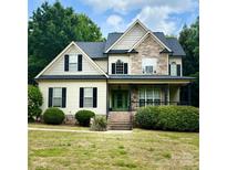 Inviting two-story home with a covered front porch, stone accents, manicured landscaping, and a vibrant green front door at 3320 Harvey Ln, Monroe, NC 28110