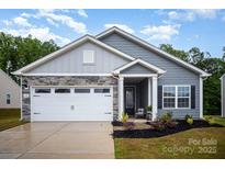 Charming gray home featuring a two-car garage, stone accents, manicured lawn and covered front porch entrance at 107 S Sina St, Troutman, NC 28166