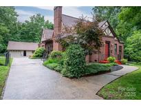 Charming brick Tudor-style home with a red door, lush landscaping, and a detached garage at 1136 S Edgemont Ave, Gastonia, NC 28054