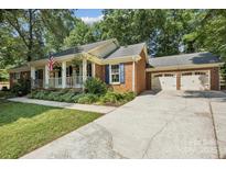 Charming brick home featuring an inviting front porch, well-manicured landscaping, and an attached two-car garage at 405 Scarborough Ln, Matthews, NC 28105