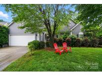 Charming gray home featuring a two-car garage, a well-manicured lawn and a cozy front porch with red adirondack chairs at 6717 Bickham Ln, Charlotte, NC 28269