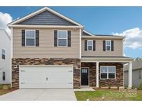 Two-story home featuring a white garage door, tan siding, stone accents, and black shutters against a clear blue sky at 4016 Cramer Estates Ct, Gastonia, NC 28056