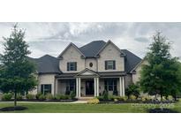 Elegant gray brick home with a covered front porch, black shutters, and lush landscaping creates curb appeal at 1152 Grand Oak Dr, Waxhaw, NC 28173