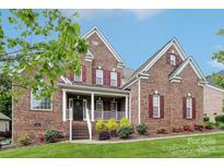 Charming two-story brick home with red shutters, a covered porch, and well-maintained landscaping at 9034 Kensington Forest Dr, Harrisburg, NC 28075