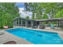 A beautiful backyard pool featuring a patio seating area in a lush, wooded setting at 447 Merwick Cir, Charlotte, NC 28211