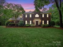 Beautiful brick two-story home with a well-manicured lawn and mature trees during dusk at 8527 Foxbridge Dr, Matthews, NC 28104