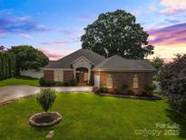 Charming brick home with a lush lawn, manicured landscaping, and a well-lit driveway at twilight at 133 43Rd Avenue Nw Ln, Hickory, NC 28601