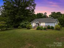 Quaint home with a beautiful lawn, mature trees, and a lovely covered porch at sunset at 5371 Davidson Rd, Davidson, NC 28036