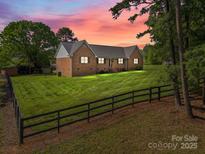 Charming brick home boasts a metal roof and expansive lawn, framed by mature trees and a classic wooden fence at 425 Troutman Rd, Rockwell, NC 28138